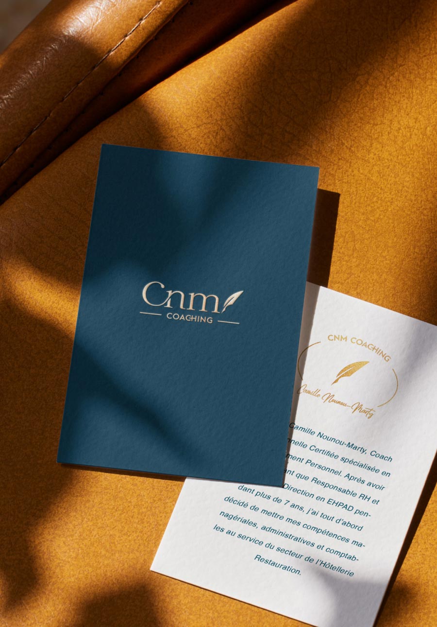 Cartes graphiques bleu et blanches avec le logotype Cnm Coaching. Les cartes sont posées sur un siège jaune.